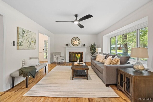 living area featuring a fireplace, light wood-style flooring, a ceiling fan, and baseboards
