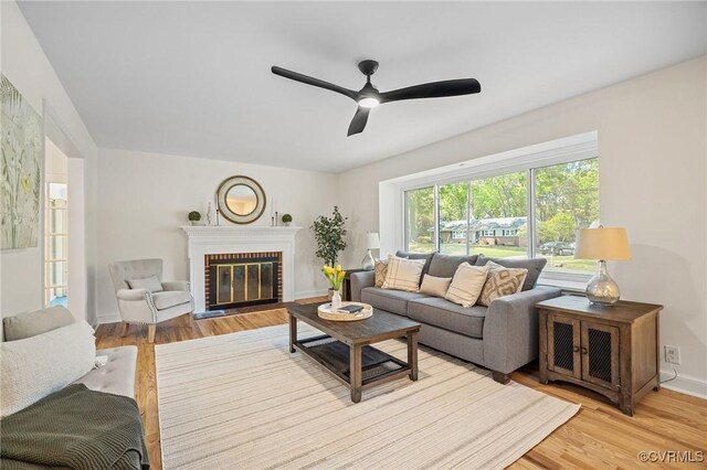 living area with light wood-style floors, a brick fireplace, a ceiling fan, and baseboards