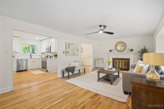 living area featuring a fireplace, light wood finished floors, baseboards, and a ceiling fan