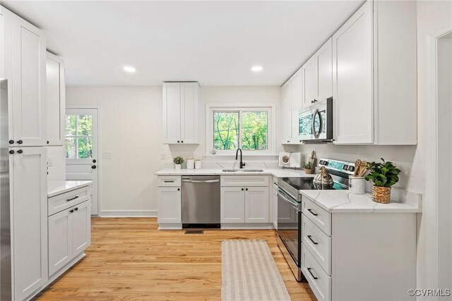 kitchen featuring white cabinets, light wood-style floors, stainless steel appliances, and a sink