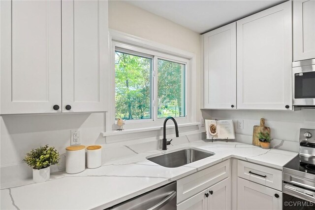 kitchen with appliances with stainless steel finishes, light stone countertops, a sink, and white cabinetry