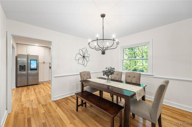 dining area featuring light wood finished floors, baseboards, and a notable chandelier