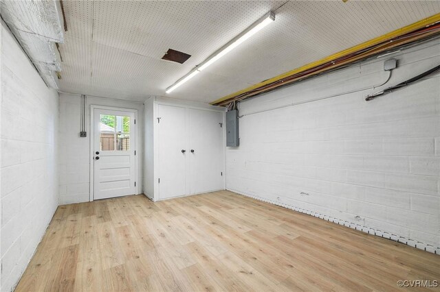below grade area featuring light wood-style floors, electric panel, and concrete block wall