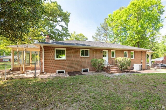 back of property with central air condition unit, a chimney, fence, brick siding, and a yard