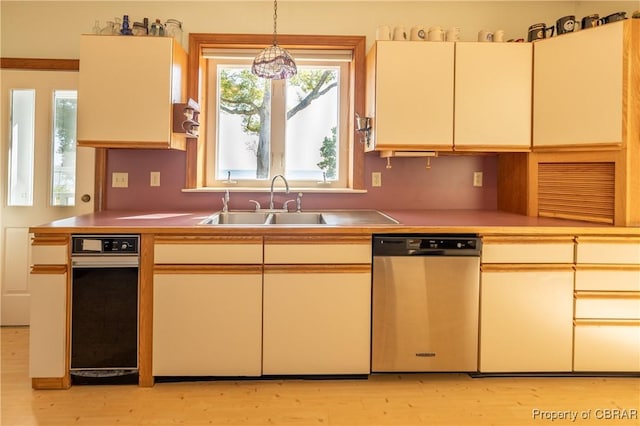 kitchen with light wood-type flooring, stainless steel dishwasher, a sink, and cream cabinets