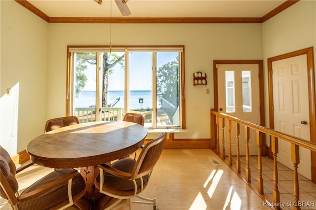 dining area with a ceiling fan, baseboards, crown molding, and a water view
