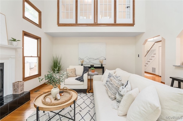 living area with a towering ceiling, wood finished floors, a fireplace, stairway, and arched walkways