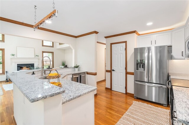 kitchen featuring appliances with stainless steel finishes, a peninsula, light wood-style floors, white cabinetry, and crown molding