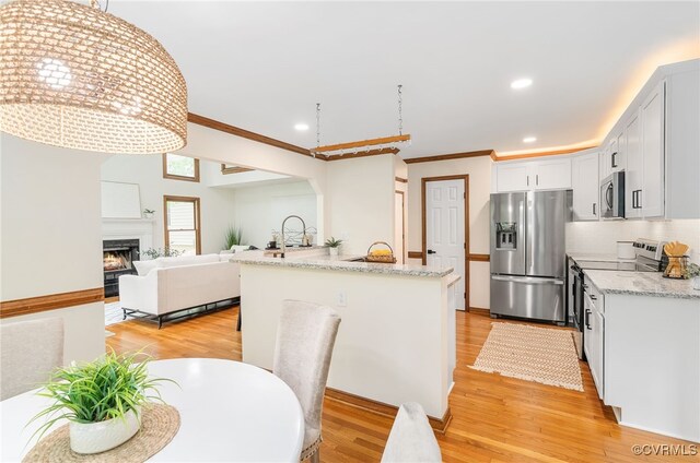 kitchen featuring stainless steel appliances, crown molding, light wood finished floors, a lit fireplace, and tasteful backsplash