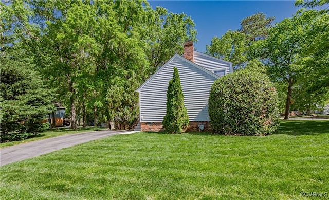 exterior space featuring crawl space, aphalt driveway, a yard, and a chimney