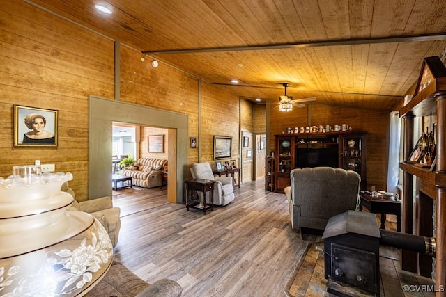 living area featuring vaulted ceiling, wood finished floors, ceiling fan, wood ceiling, and wooden walls
