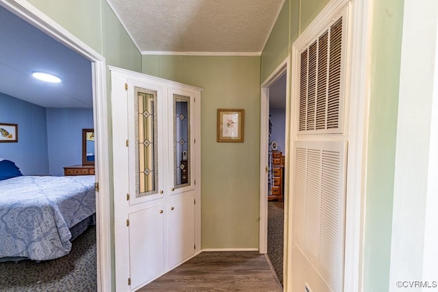 hallway with crown molding, a heating unit, dark wood-type flooring, and a textured ceiling