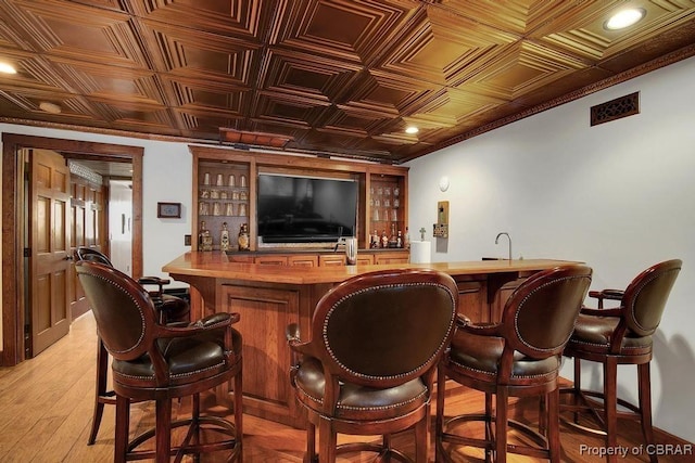 bar featuring indoor wet bar, an ornate ceiling, and light wood-style floors
