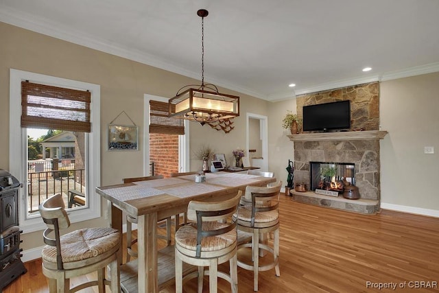 dining area featuring a stone fireplace, crown molding, wood finished floors, and baseboards
