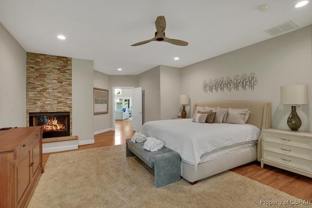 bedroom with a multi sided fireplace, wood finished floors, ceiling fan, visible vents, and recessed lighting