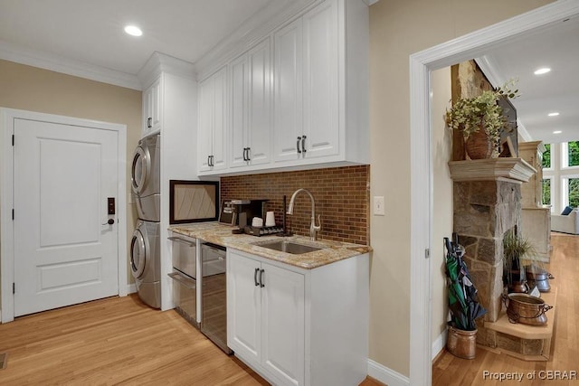laundry room with laundry area, a sink, light wood-style floors, crown molding, and stacked washer and dryer