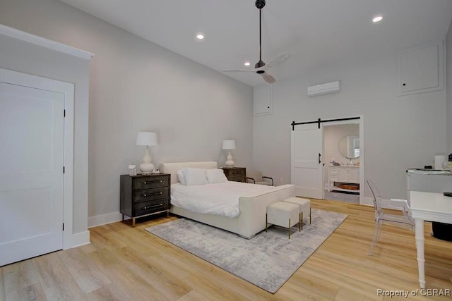 bedroom with a barn door, an AC wall unit, baseboards, and light wood-type flooring