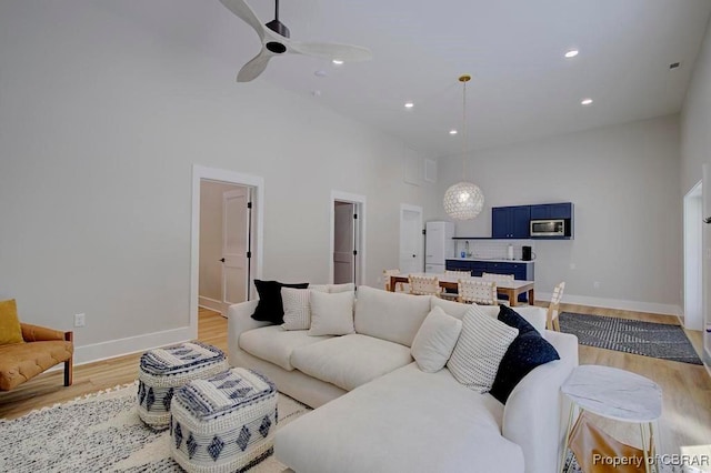 living area with recessed lighting, a ceiling fan, baseboards, light wood-style flooring, and high vaulted ceiling