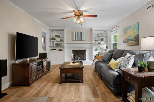 living area featuring a ceiling fan, a fireplace with raised hearth, light wood-type flooring, built in features, and crown molding