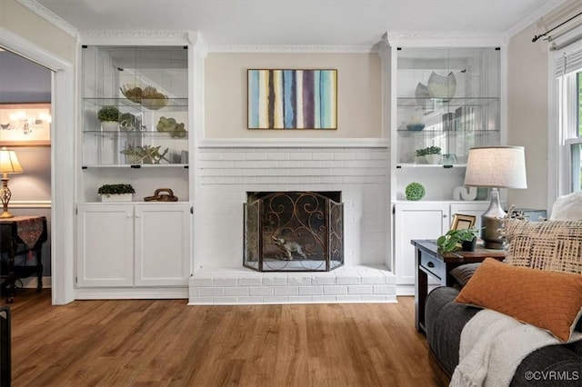 living area featuring wood finished floors, crown molding, a fireplace, and built in shelves
