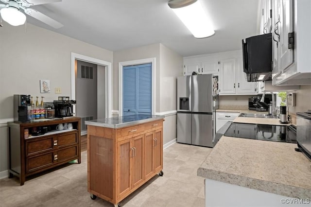 kitchen featuring stainless steel fridge with ice dispenser, a ceiling fan, light countertops, a sink, and a center island