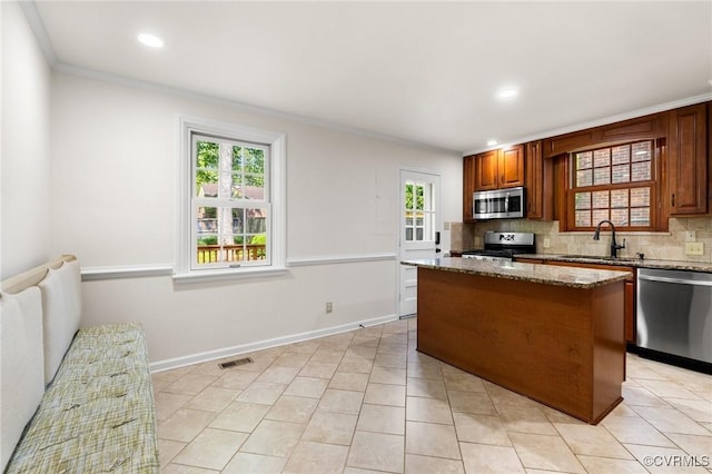 kitchen with tasteful backsplash, crown molding, a sink, appliances with stainless steel finishes, and a kitchen island
