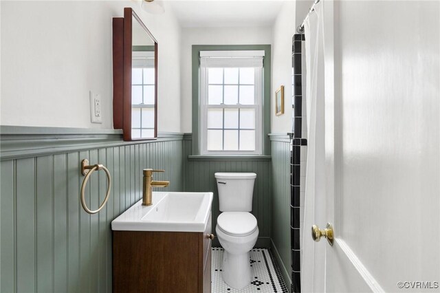 bathroom with toilet, tile patterned floors, wainscoting, and vanity