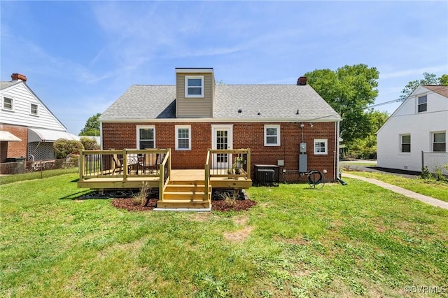 back of property with a wooden deck, cooling unit, roof with shingles, brick siding, and a yard