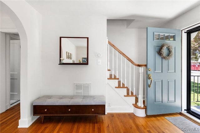 entrance foyer featuring arched walkways, baseboards, wood finished floors, visible vents, and stairway