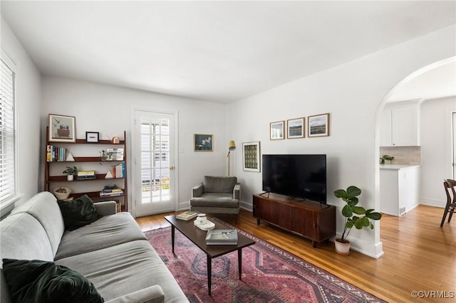 living area featuring baseboards, arched walkways, and light wood finished floors