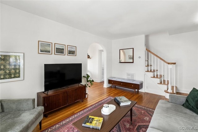living room featuring visible vents, stairs, wood finished floors, baseboards, and arched walkways