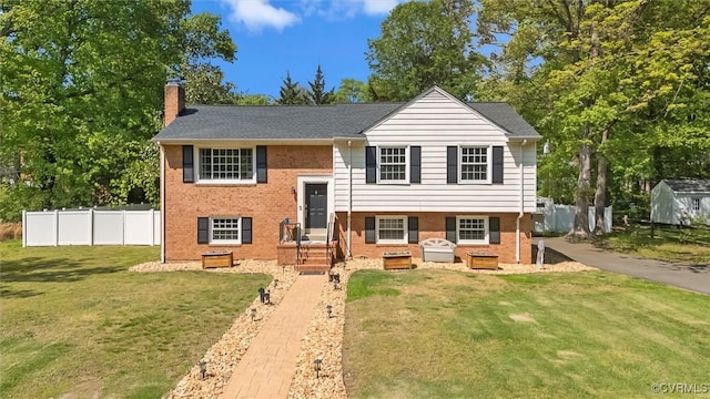 split foyer home featuring brick siding, fence, a front lawn, and a chimney