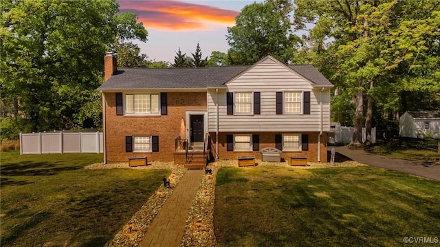 raised ranch featuring entry steps, a chimney, fence, brick siding, and a front lawn
