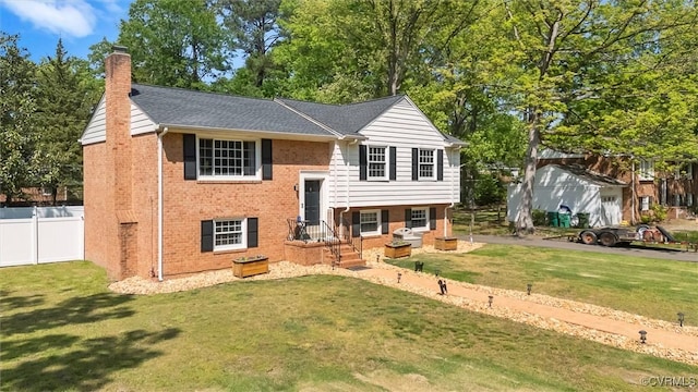 bi-level home featuring brick siding, fence, a front lawn, and a chimney