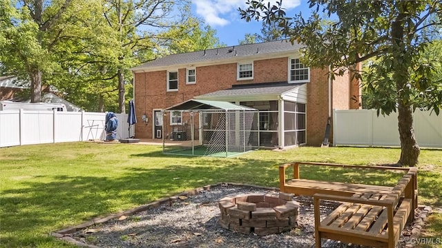 rear view of house featuring a lawn, a fire pit, a fenced backyard, and a sunroom