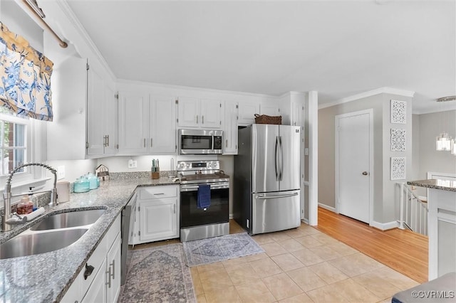 kitchen featuring light stone counters, stainless steel appliances, a sink, white cabinetry, and crown molding