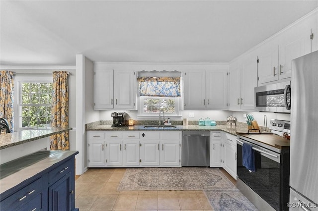 kitchen featuring a sink, stainless steel appliances, light tile patterned floors, light stone counters, and white cabinets