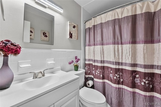 bathroom featuring tile walls, a wainscoted wall, toilet, vanity, and curtained shower