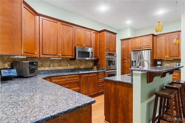 9522 Nassington Ct, Henrico, VA 23229 - kitchen featuring appliances with stainless steel finishes, a breakfast bar area, a sink, decorative backsplash, and brown cabinetry