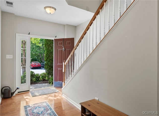 foyer entrance featuring visible vents, baseboards, wood finished floors, and stairway