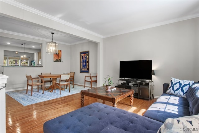 living area with baseboards, ornamental molding, wood finished floors, and a notable chandelier