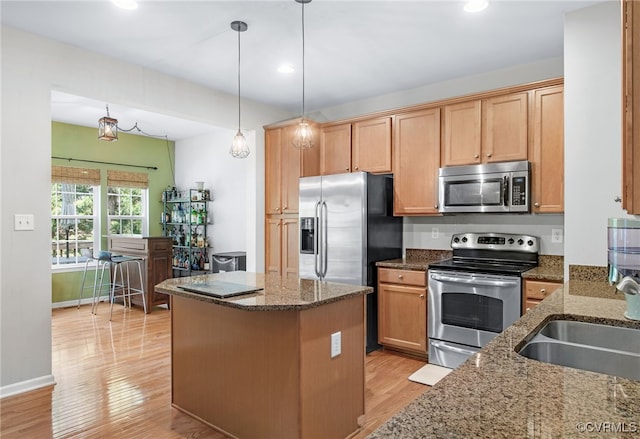 kitchen with light wood-style floors, a center island, a sink, dark stone countertops, and appliances with stainless steel finishes