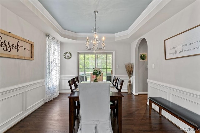 dining space featuring arched walkways, a notable chandelier, a decorative wall, and a tray ceiling