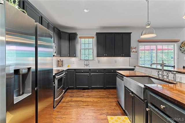 kitchen with a sink, decorative backsplash, dark wood-type flooring, pendant lighting, and appliances with stainless steel finishes