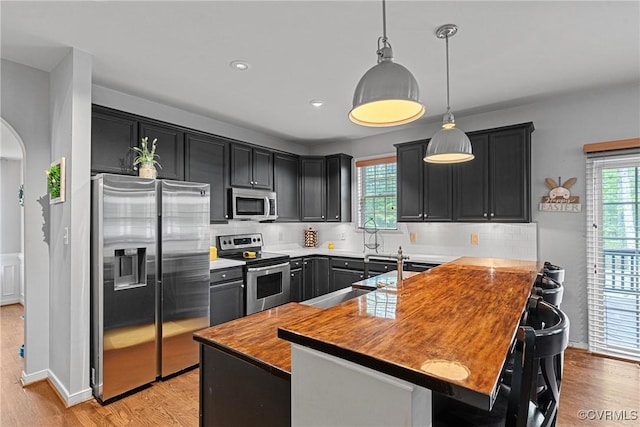 kitchen with a wealth of natural light, appliances with stainless steel finishes, light wood-style flooring, and decorative backsplash