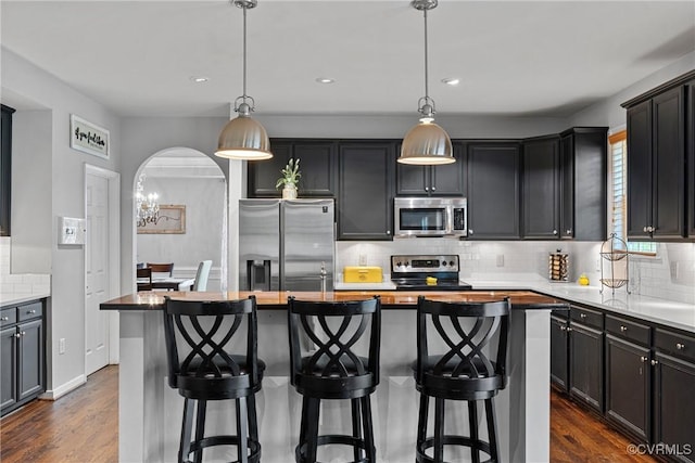 kitchen featuring dark wood finished floors, a kitchen island, stainless steel appliances, and decorative backsplash