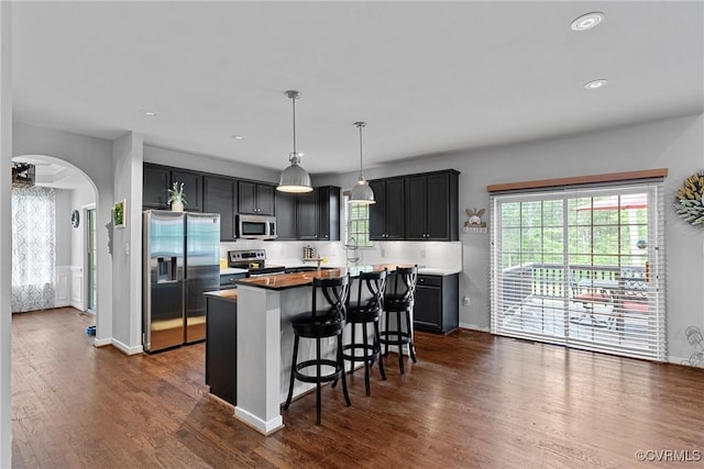 kitchen featuring appliances with stainless steel finishes, dark wood-type flooring, arched walkways, and a center island