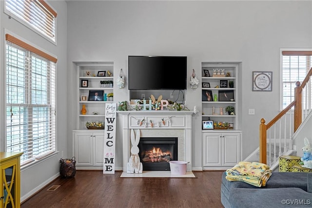 living area with a high end fireplace, visible vents, built in features, and dark wood finished floors