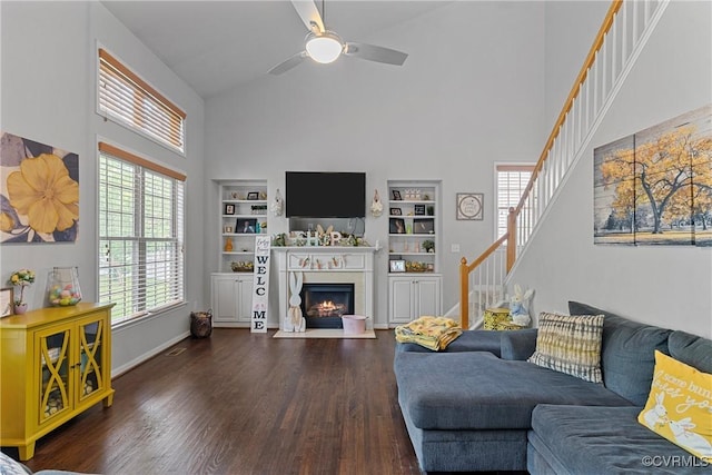 living room with a fireplace with flush hearth, stairway, ceiling fan, dark wood-style floors, and high vaulted ceiling