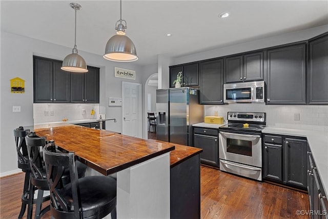 kitchen with dark wood finished floors, decorative backsplash, butcher block counters, stainless steel appliances, and decorative light fixtures